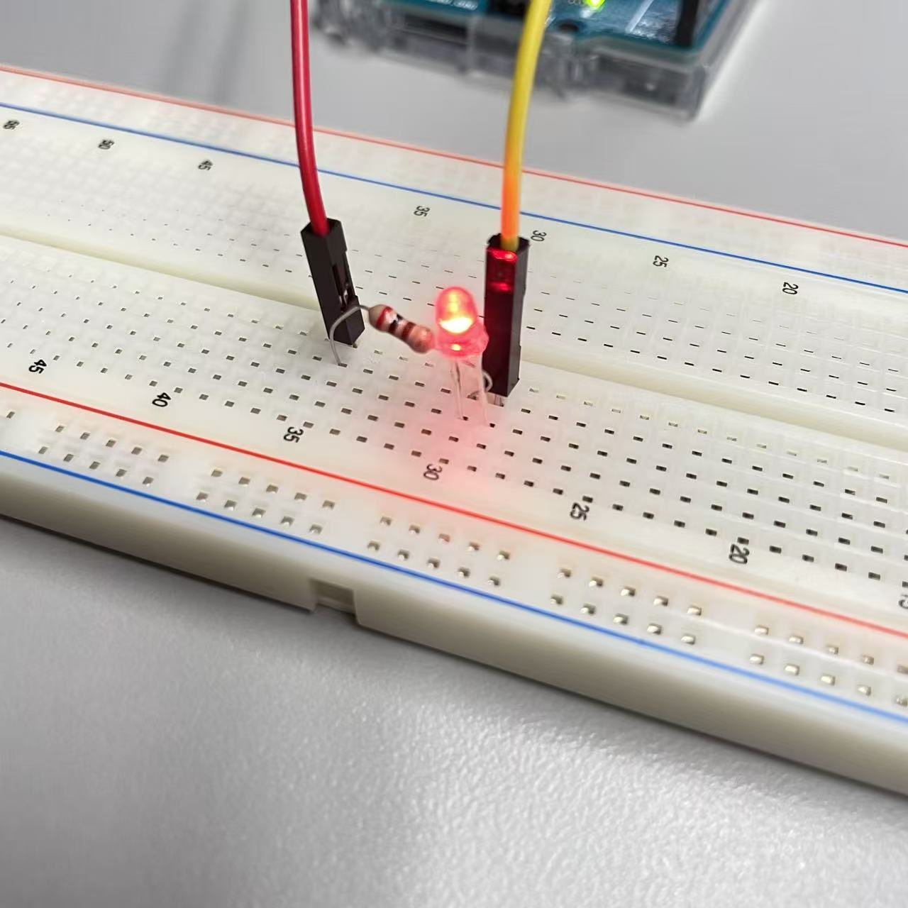 A red LED light on a breadboard connected with wires and a resistor, powered by an Arduino and successfully illuminated.